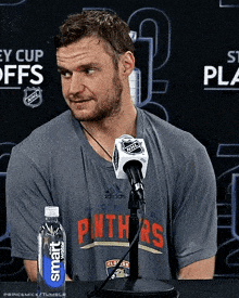 a man wearing a shirt that says panthers is sitting in front of a microphone