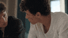 a man in a white t-shirt looks at another man in a black jacket
