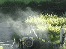 a yellow tractor is spraying a field with smoke