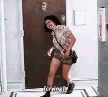 a woman is standing in a hallway and crying while holding a purse .
