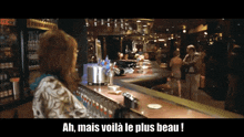 a woman standing at a bar with the words " ah mais voila le plus beau " above her