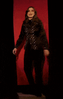a woman in a black shirt and black pants is standing in front of a red wall