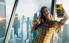 a woman taking a selfie in front of a window with a city in the background
