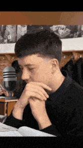 a young man sits in front of a microphone with his hand on his chin