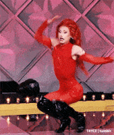 a drag queen in a red outfit and black boots is dancing on stage .
