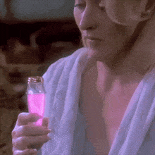 a woman in a bathrobe is holding a bottle of pink liquid