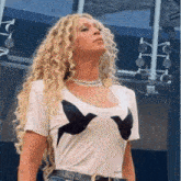 a woman with blonde curly hair is wearing a white t-shirt with birds on it