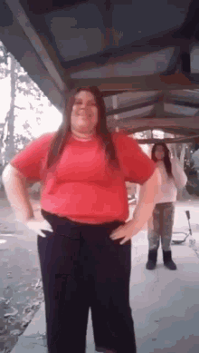 a woman in a red shirt and black pants is standing with her hands on her hips