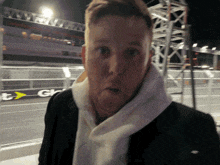 a man wearing a white scarf stands in front of a sign that says gt