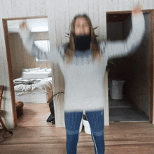 a woman in a grey sweater is standing in a room with her arms up