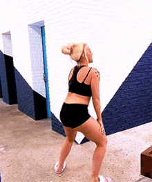 a woman in a black top and black shorts is dancing in front of a brick wall