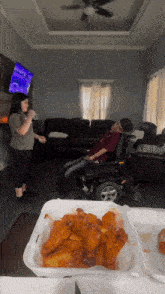 a woman singing into a microphone while a man in a wheelchair eats chicken wings