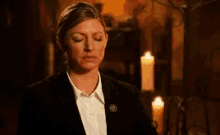 a woman in a suit and white shirt is standing in a dark room with candles .