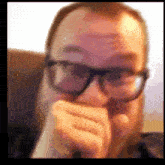 a man wearing glasses is covering his face with his hand