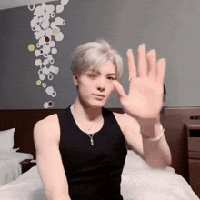 a man in a black tank top is sitting on a bed waving his hand