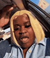 a woman with blonde hair is sitting in a car and making a funny face .