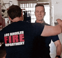 two men wearing los angeles fire department shirts are hugging each other