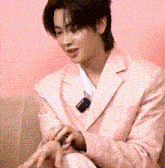 a young man in a pink suit is sitting on a couch with his hands on his lap .