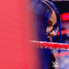 a woman with blue hair and glasses is standing in a wrestling ring