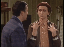two men are talking in a living room with a clock on the wall that says ' army '