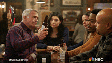 a group of people are sitting at a table with a man holding a bottle of beer in front of them