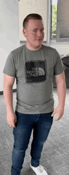 a young man wearing a t-shirt and jeans is standing in a room .