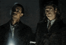 two men in suits are standing next to each other in a dark room .