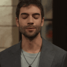 a man with his eyes closed wearing a suit and necklace
