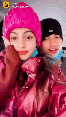 a girl wearing a pink beanie is standing next to another girl wearing a mask