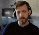 a man with a beard wearing headphones in front of a tv that says icons of the realms