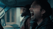 a man with a beard is screaming while driving a car