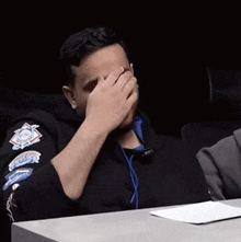 a man is covering his face with his hand while wearing a black jacket with patches on it