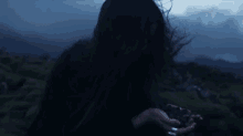 a woman with long black hair is standing in a field at night holding a rock .