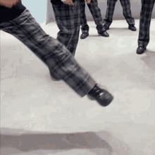 a person wearing plaid pants and black shoes is standing on a white floor .