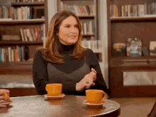 a woman sits at a table with two cups of orange coffee