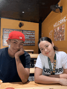 a man and a woman are sitting at a table in front of a welcome sign