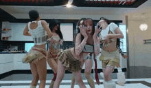 a group of women are dancing in a kitchen and one of them is covering her face with her hand