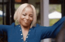 a woman in a blue shirt is dancing with her arms outstretched and smiling .