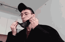 a man wearing glasses and a black hat is putting on a black face mask