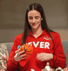 a woman in a red jacket with the word ever on it is holding a basketball .