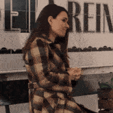 a woman in a plaid coat is sitting in front of a sign that says rein