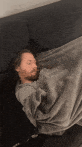 a man with a beard is sleeping on a black couch