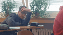 a man wearing glasses sits at a desk with his hand on his face