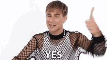 a man wearing a fishnet top is giving a thumbs up and saying yes .