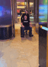 a man pushing another man in a wheelchair who is wearing a t-shirt that says raja