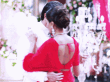 a woman in a red dress is hugging a man in a white shirt .
