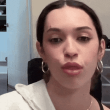 a woman wearing hoop earrings and a white hoodie looks at the camera