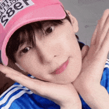 a young man wearing a pink hat and a blue jacket is making a face with his hands .