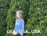 a little girl in a blue shirt stands in front of a bush with the words usa usa usa written on it