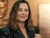 a woman wearing a black leather jacket is smiling in front of a sign that says ' emirates '